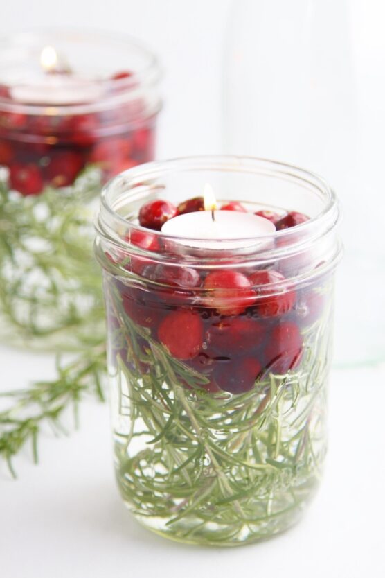Floating candles with rosemary sprigs and cranberries inside glass jars