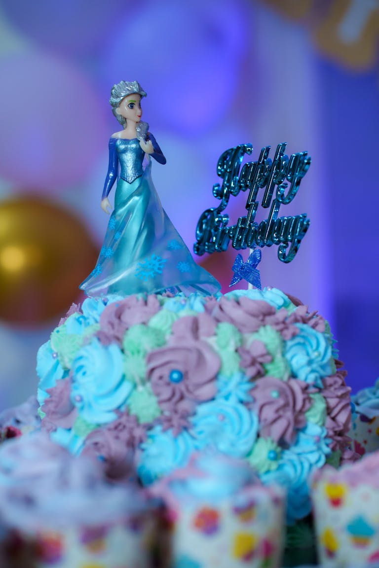 A Frozen-themed birthday cake with an intricate doll topper in vibrant colors, perfect for a child's celebration.