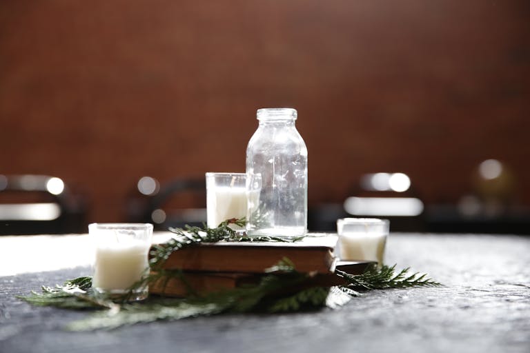 A rustic scene featuring a vintage glass bottle, candles, and greenery on a book.