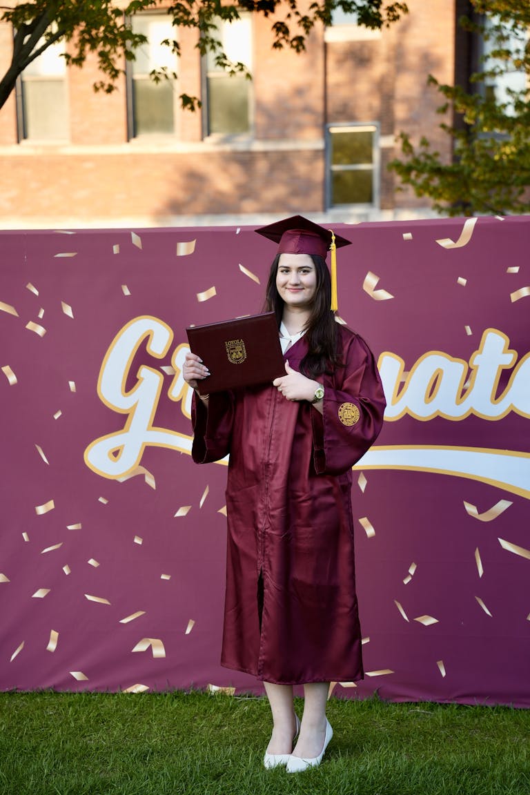 A young woman celebrates graduation with a diploma in hand against a festive backdrop.