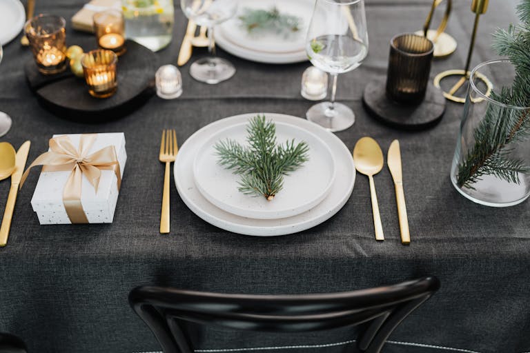 Sophisticated holiday table setting with pine decor and golden utensils, perfect for Christmas gatherings.